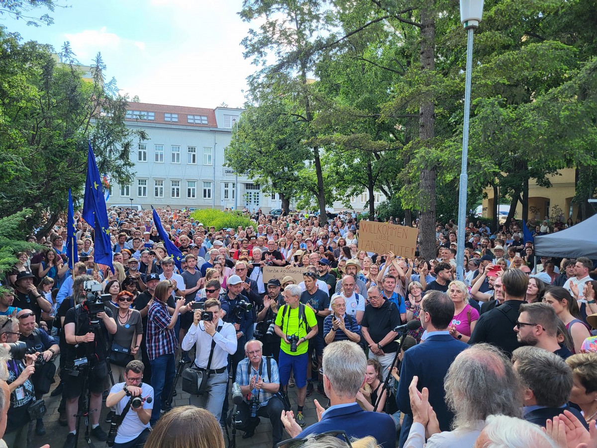 Skupina lidí, lze rozpoznat předsedu senátu Miloše Vystrčila. V davu je vidět transparent „Willkomenn liebe Landsleute“ (Vítejte, milí krajané).
